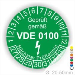 Prüfaukleber rund Farbe- Grün, Text "Geprüft gemäß VDE 0100" in Weiß danach ein Elektro- Pfeil in Weiß, Startjahr- 27, Monatszahlen Oben und Jahreszahlen Unten in Kreisform. Über den Jahreszahlen Text "Nächster Prüftermin"