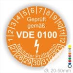 Prüfaukleber rund, Farbe- Orange, Text "Geprüft gemäß VDE 0100" in Weiß danach ein Elektro- Pfeil in Weiß, Startjahr- 27, Monatszahlen Oben und Jahreszahlen Unten in Kreisform. Über den Jahreszahlen Text "Nächster Prüftermin"