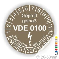 Prüfetikette rund, Farbe- Braun, Text "Geprüft gemäß VDE 0100" in Weiß danach ein Elektro- Pfeil in Weiß, Startjahr- 29, Monatszahlen Oben und Jahreszahlen Unten in Kreisform. Über den Jahreszahlen Text "Nächster Prüftermin"