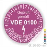 Prüfetikette rund, Farbe- Lila, Text "Geprüft gemäß VDE 0100" in Weiß danach ein Elektro- Pfeil in Weiß, Startjahr- 29, Monatszahlen Oben und Jahreszahlen Unten in Kreisform. Über den Jahreszahlen Text "Nächster Prüftermin"