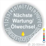 Prüfetiketten, Wartungsplakette rund, Farbe- Grau, Text "Nächste Wartung/Ölwechsel" in Weiß. Startjahr- 29, Monatszahlen Oben und Jahreszahlen Unten in Kreisform, über den Jahreszahlen ein Öltropfen als Icon/Piktogramm in Gelb.